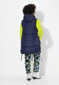 Dunjacka i marinblått, med huva och sidogångjärn, matchad med kamouflagedbyxor som har gula stjärnor och silverfärgade ankelskåpor.