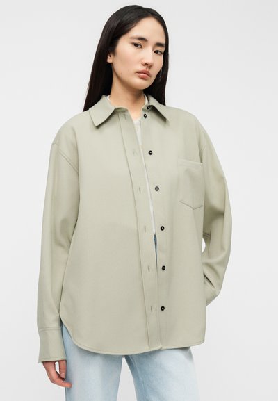 Ανοιχτό πράσινο πουκάμισο με γιακά, μακριά μανίκια, μία τσέπη στο στήθος και μαύρα κουμπιά. Μαλακό ύφασμα με ελαφρώς φαρδιά εφαρμογή.