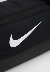 Czarna torba sportowa z tkaniny o teksturowanej powierzchni i wyraźnym białym logo Nike; posiada zamek błyskawiczny u góry.