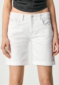 Shorts in denim bianco con orli risvoltati, dotati di tasche frontali e chiusura a bottone metallico. Texture liscia e design aderente.
