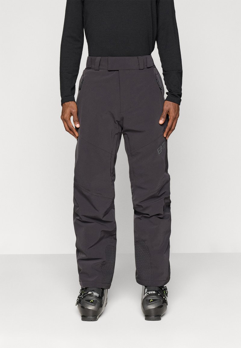 Férfi sínadrág sötétszürke színben, vízálló anyagból készült, megerősített térdekkel, egyenes szabással és oldalsó cipzáras zsebekkel rendelkezik.