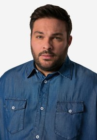 Džínová košile v tmavě modré barvě s límečkem na knoflíky, dvěma náprsními kapsami a měkkou texturou. Obsahuje světlé knoflíky.