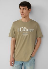 Olijfgroen T-shirt met korte mouwen en ronde hals, voorzien van witte bedrukte tekst: "s.Oliver ELEVATED ESSENTIALS SINCE 1969."