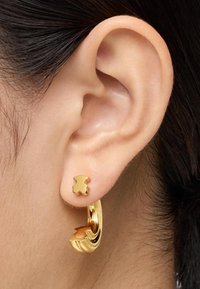 Boucles d'oreilles en or avec un clou en forme d'ours et un gros anneau au design ondulé, mettant en valeur une finition polie et une texture lisse.