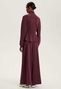 Sacou ajustat, de culoare vișinie, cu guler înalt și tiv peplum, asortat cu pantaloni cu picioare largi. Material neted, design minimalist, accesorii subtile.