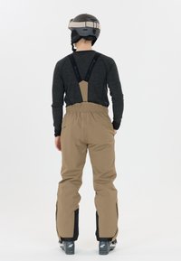 Skihose in Beige mit verstellbaren Trägern, elastischem Bund und schwarzen Akzenten an den Säumen. Strapazierfähiger Stoff und lockere Passform für Bewegungsfreiheit.