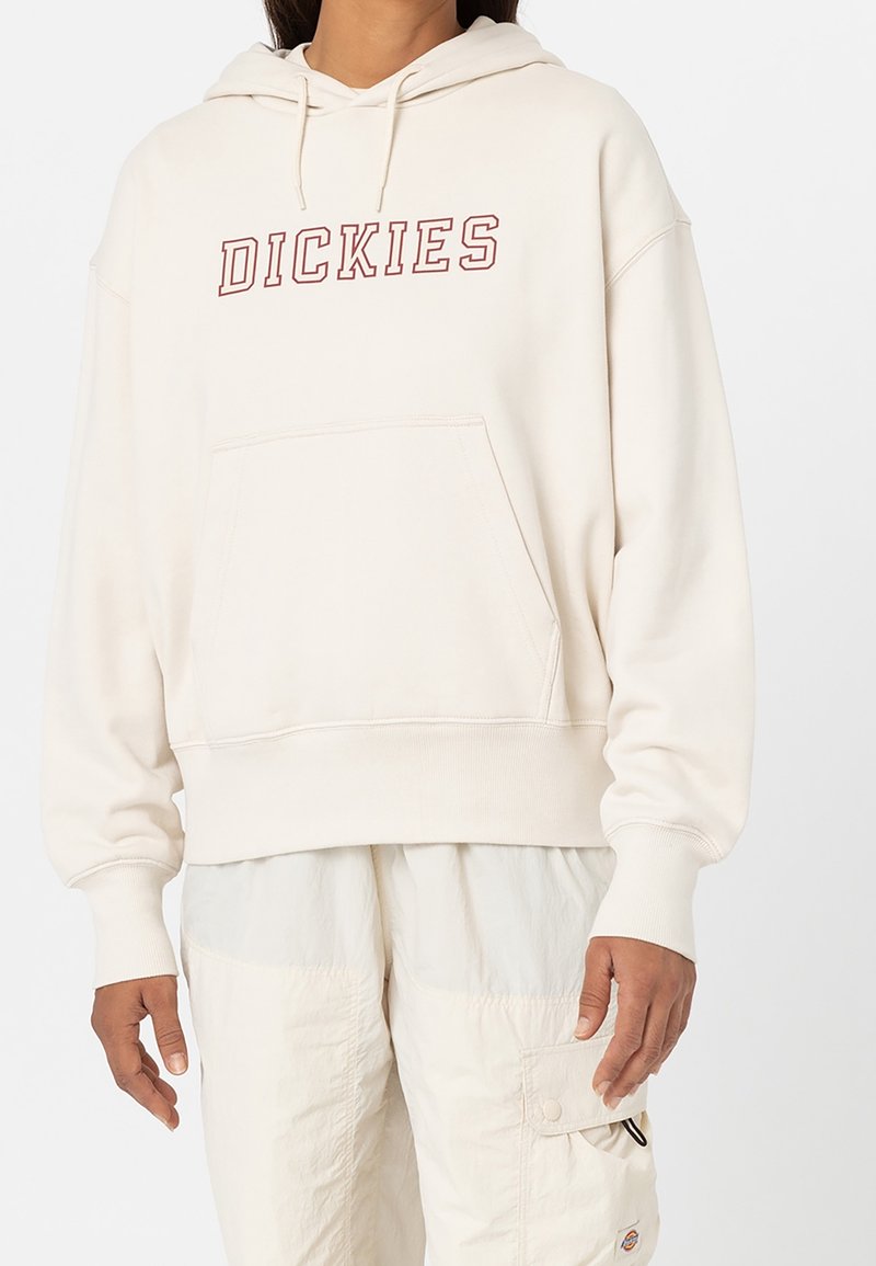 Krämfärgad huvtröja med en framficka, ribbade ärmslut och justerbar huva. "DICKIES"-logotyp i röd på bröstet, avslappnad passform.