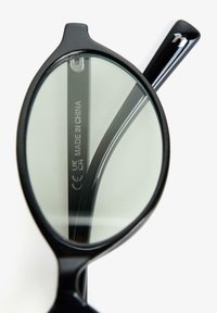 Fekete műanyag szemüvegkeret ovális lencsékkel, belső szárán "Made in China" felirattal, egyszerű fehér háttér előtt.