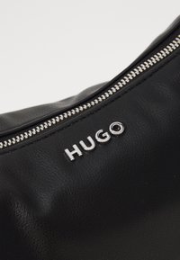 Borsa in pelle nera con zipper argentato e logo metallico "HUGO". Texture liscia con design minimalista, enfatizzando funzionalità ed eleganza.