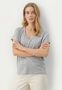 Grå V-ringad t-shirt i mjukt tyg, med korta ärmar och avslappnad passform, bärs med krämfärgade byxor.