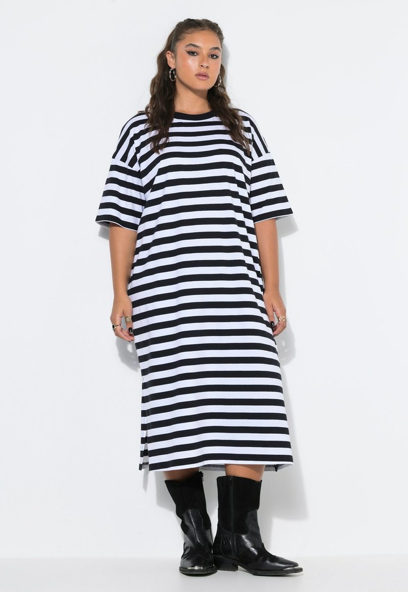 Woman wearing a black and white horizontal striped midi dress and black mid-calf boots standing against a white background.