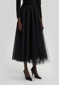 Zwarte tule rok met een volumineus, gelaagd ontwerp. Elastische tailleband, knielengte, gecombineerd met puntige zwarte hakken.