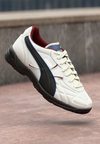 Valged tennisajalatsid mustade ja siniste aktsentidega, tekstureeritud nahk pealmine osa, punane sisemus ja valged paelad. Omab pehmendatud talda ja stiilset disaini.