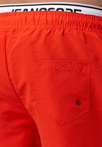 Shorts de bain rouges avec une finition texturée, taille élastique et une poche arrière dotée de coutures horizontales et d'un détail à pression.
