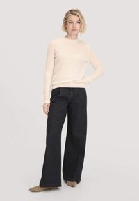 Cremefarbener Pullover mit rundem Ausschnitt, kombiniert mit hochtaillierten, weiten, dunkelblauen Jeans. Glatte Textur und schmal geschnittene Ärmel.