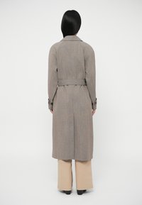 Γκρι καρό παλτό τρανς με ζώνη στη μέση, μανσέτες με κουμπιά και σχισμή στο πίσω μέρος. Λεία υφή, μακριά μανίκια και μήκος μέχρι τη μέση της γάμπας.