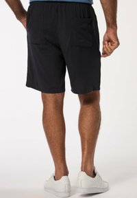 Pantaloni corti neri con elastico in vita e due tasche posteriori, mostrati da dietro, abbinati a sneakers bianche basse.