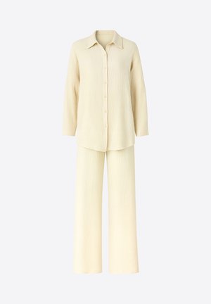 Cremefarbenes zweiteiliges Outfit mit einem Hemd zum Knöpfen, Kragen und langen Ärmeln, kombiniert mit weit geschnittenen Hosen aus strukturiertem Stoff.