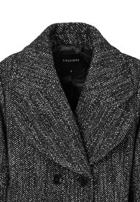 Cappotto in bianco e nero a motivo houndstooth con un grande collo, chiusura doppiopetto e bottoni neri. L'interno foderato è visibile. Taglia S.
