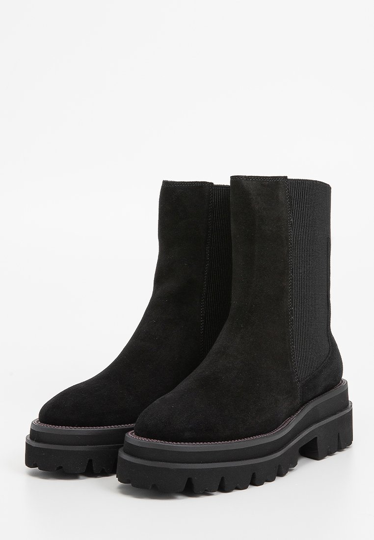 Stivali neri in suede alla caviglia con pannelli laterali elasticizzati, suole in gomma spessa e una finitura texturizzata. Parte superiore liscia con accenti cuciti.