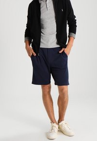 Navy shorts made of cotton blend fabric, paired with a gray polo shirt and a black jacket. White sneakers complete the outfit.
