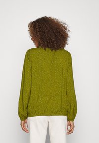 Blusa verde con estampado que presenta un dobladillo elástico y mangas largas, hecha de un material ligero con una textura suave.