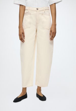 Beige High-Waist-Jeans mit weitem Bein, aufgesetzten Fronttaschen, kombiniert mit schwarzen Ballerinas und einem weißen Kurzarm-Top.