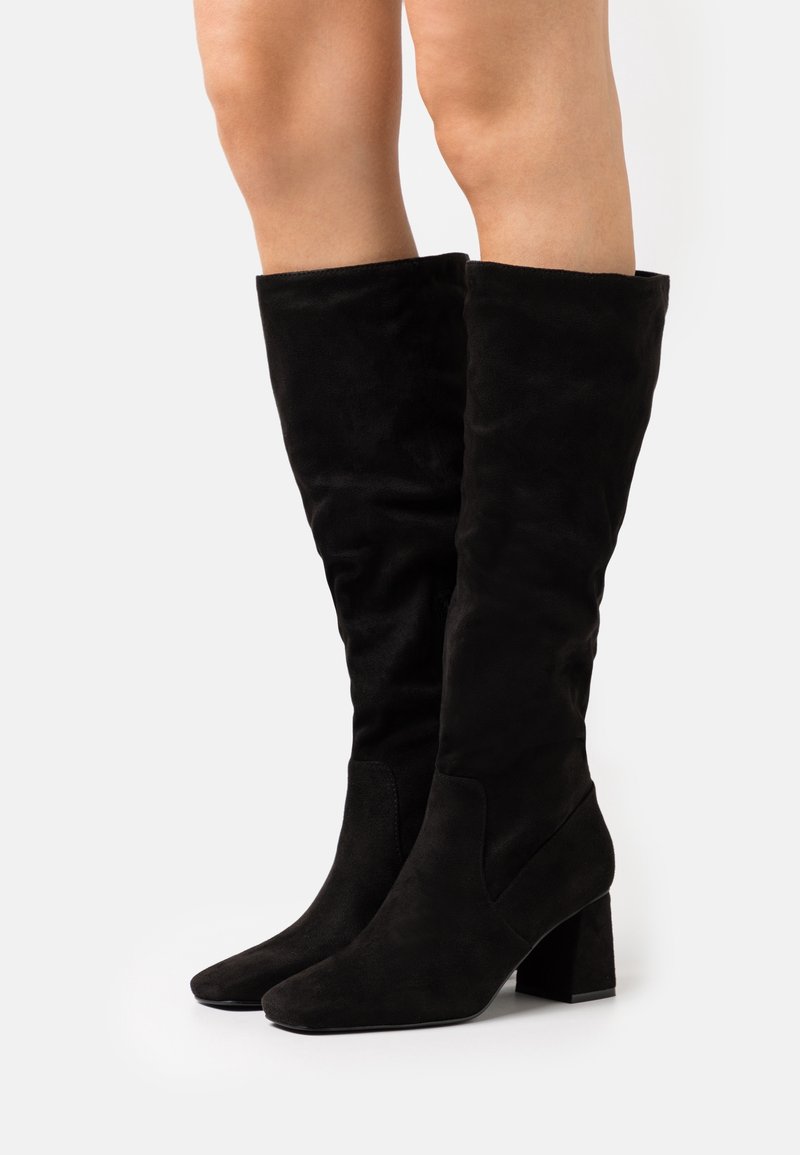 Schwarze Wildlederkniehohe Stiefel mit Blockabsatz, spitzen Zehen und glatter Oberfläche, die ein tailliertes Design aufweisen, das sich an das Bein anpasst.