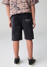 Čierne bavlnené šortky so šitým lemom, s vreckom na zadnej strane s bielym nápisom „ALLSAINTS“. Kombinované s čiernymi teniskami.