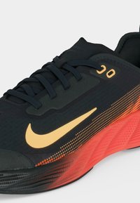 Μαύρο και πορτοκαλί παπούτσι τρεξίματος Nike με κίτρινο λογότυπο swoosh, μαύρα κορδόνια και υφασμένο πέλμα, γωνιακό για να δείξει πλάγια και πάνω όψη.