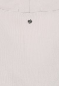 Light beige fabric with subtle texture and a small round metal button stitched near the top center with faint engraved text.