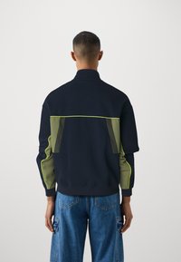 Casaco de fecho navy com painéis em verde e costura neon, apresenta um colarinho elevado e um corte descontraído, feito de material texturizado.