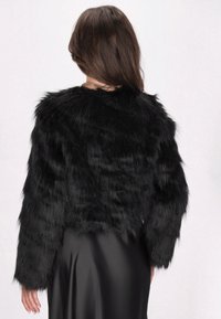 Zwarte nepbonten cropped jacket met lange mouwen en een zachte, textuurfinish, gedragen over een glad, zwart satijnen jurkje.