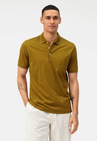 Olijfgroen poloshirt met een drieknoopsluiting, zak en witte accentstiksel. Korte mouwen en een zachte, lichtgewicht stof.