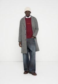 Hõbedasest kalasaba mustriga villane mantel, punane dressipluus kuldse tikandiga, laiad sinised teksad, pruunid kingad ja kreemjas kootud müts.