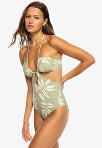 Groene een-delig badpak met witte bladerenprint, met een sleutelgat uitsnede, halterbandjes en geplooide details op de buste. Zachte textuur.