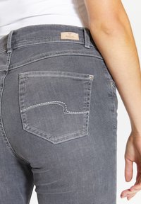 Graue Denim-Jeans mit einem enganliegenden Design, Gesäßtaschen mit dekorativer Stickerei und einem Etikett mit der Aufschrift "Angels" am Bund.