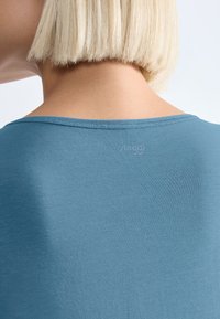 Lyseblå t-shirt med rund halsudskæring, blød tekstur og et diskret logo på bagsiden nær halsen. Korte, lige ærmer.