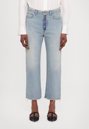 Hellblaue Jeans mit hoher Taille, fünf Knöpfen und rohem Saum. Kombiniert mit schwarzen flachen Schuhen.