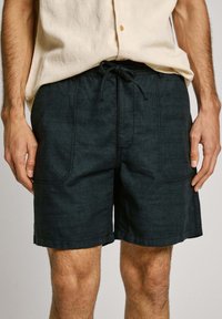 Pantalones cortos de mezclilla oscura con una textura ligera, que cuentan con una cintura ajustable, bolsillos delanteros y detalles de costura en contraste.