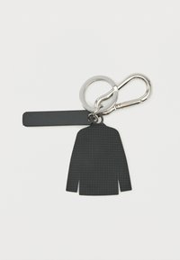 Μπρελόκ σε σχήμα μαύρου υφασμάτινου σακακιού με ορθογώνια ετικέτα προσαρτημένη σε ασημένιο κρίκο κλειδιών και κλιπ καραμπίνερ σε λευκό φόντο.
