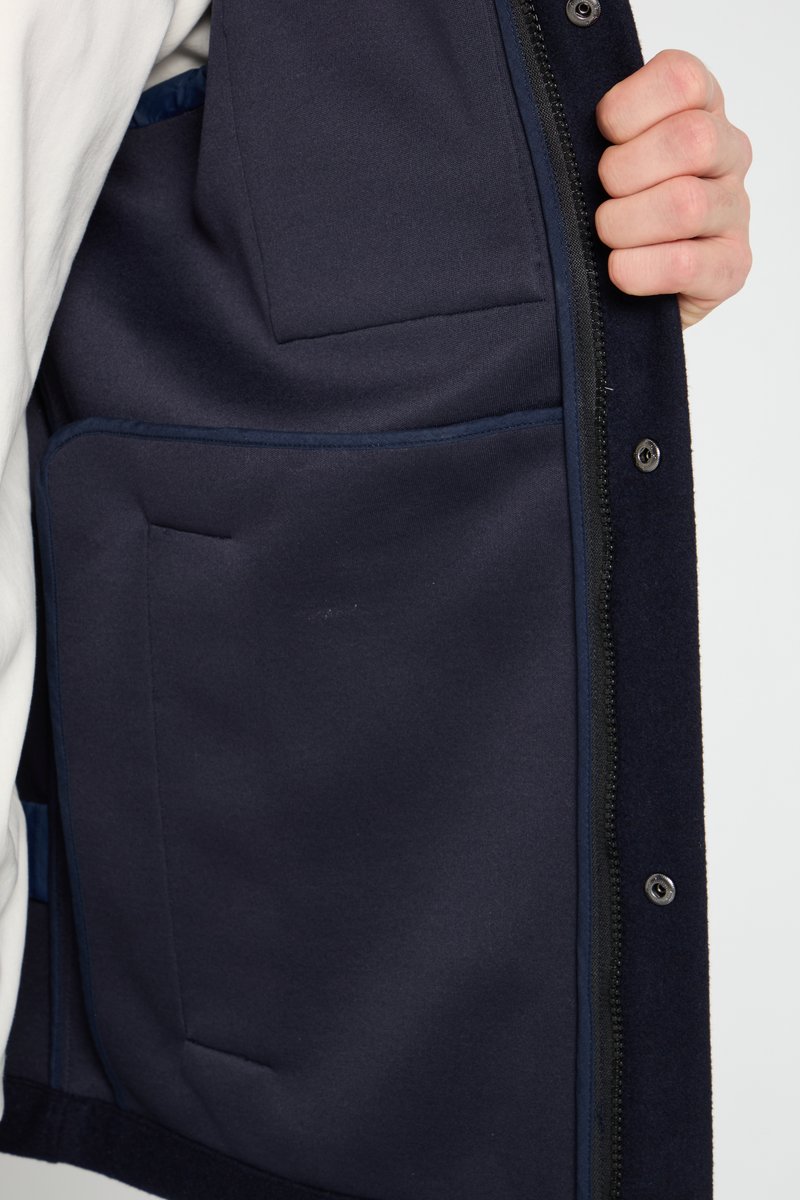 Marinejacke mit einem durchgehenden Reißverschluss und mehreren Taschen. Das Innenfutter besteht aus einem glatten Stoff, in einer einfarbigen Marinefarbe mit Knopfakzenten.