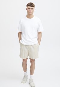 Hvit bomull T-skjorte med korte ermer, sammen med beige teksturerte shorts og hvite sneakers. Enkelt design med en avslappet passform.