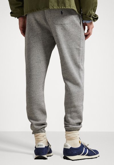 Grå sweatpants med en tætsiddende design, blødt stof, baglomme og broderet logo-detalje. Sammen med blå sportssko og lyse sokker.