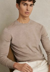 Beige gebreide trui, ronde halslijn, lange mouwen met geribbelde manchetten. Slank design, zachte textuur, gedragen met lichte broek.