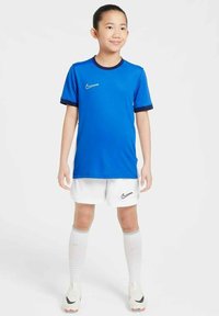 Jersey deportivo azul de Nike con acentos azul oscuro, combinado con pantalones cortos y calcetines blancos. El conjunto incluye un pequeño logo de Nike en la camiseta y los pantalones cortos.