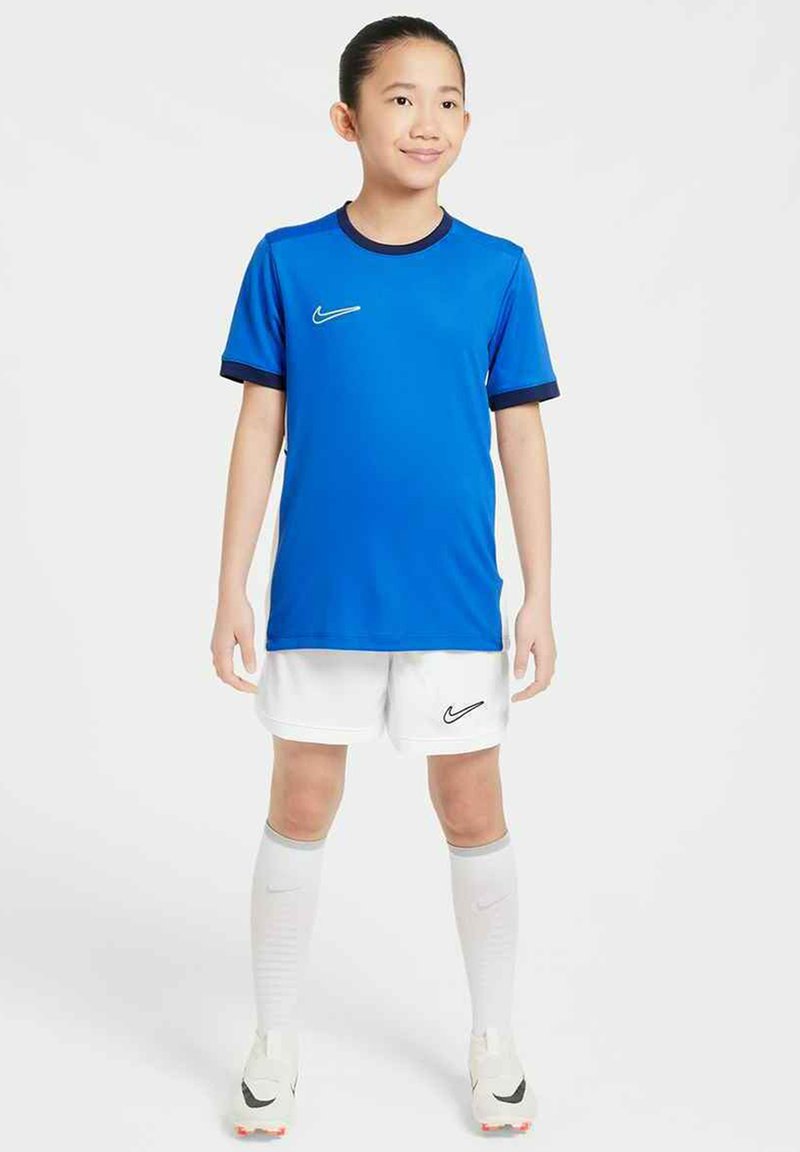 Jersey deportivo azul de Nike con acentos azul oscuro, combinado con pantalones cortos y calcetines blancos. El conjunto incluye un pequeño logo de Nike en la camiseta y los pantalones cortos.