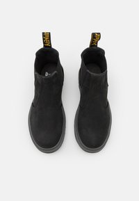 Bottines noires avec une finition en daim lisse, des panneaux latéraux élastiques et un intérieur rembourré noir. Dotées d'une tirette jaune à l'arrière.
