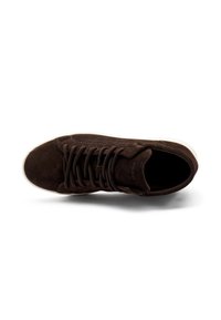 Zapatilla de ante marrón con puntera redonda, cordones en la parte delantera y suela de goma blanca. Presenta un logotipo sutil y un contraste de texturas en la parte superior.