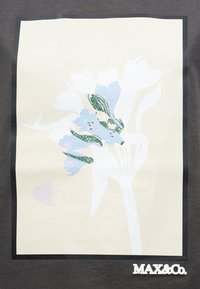 Αφηρημένη εκτύπωση με λουλούδια σε απαλό γαλάζιο και πράσινα φύλλα σε ανοιχτό μπεζ φόντο, πλαισιωμένη από μαύρο περίγραμμα, με το κείμενο «MAX&Co.» από κάτω.